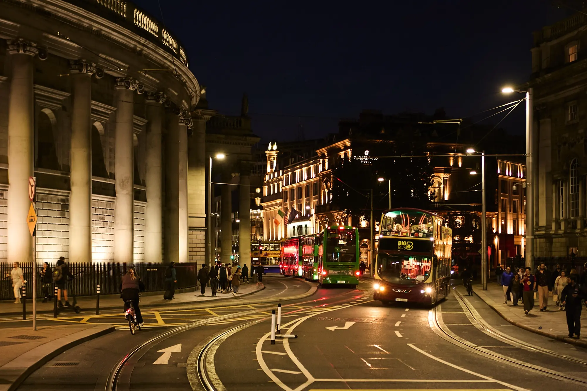 Buses and cyclists passing the colonnade of the Bank of Ireland at College Green in Dublin at night